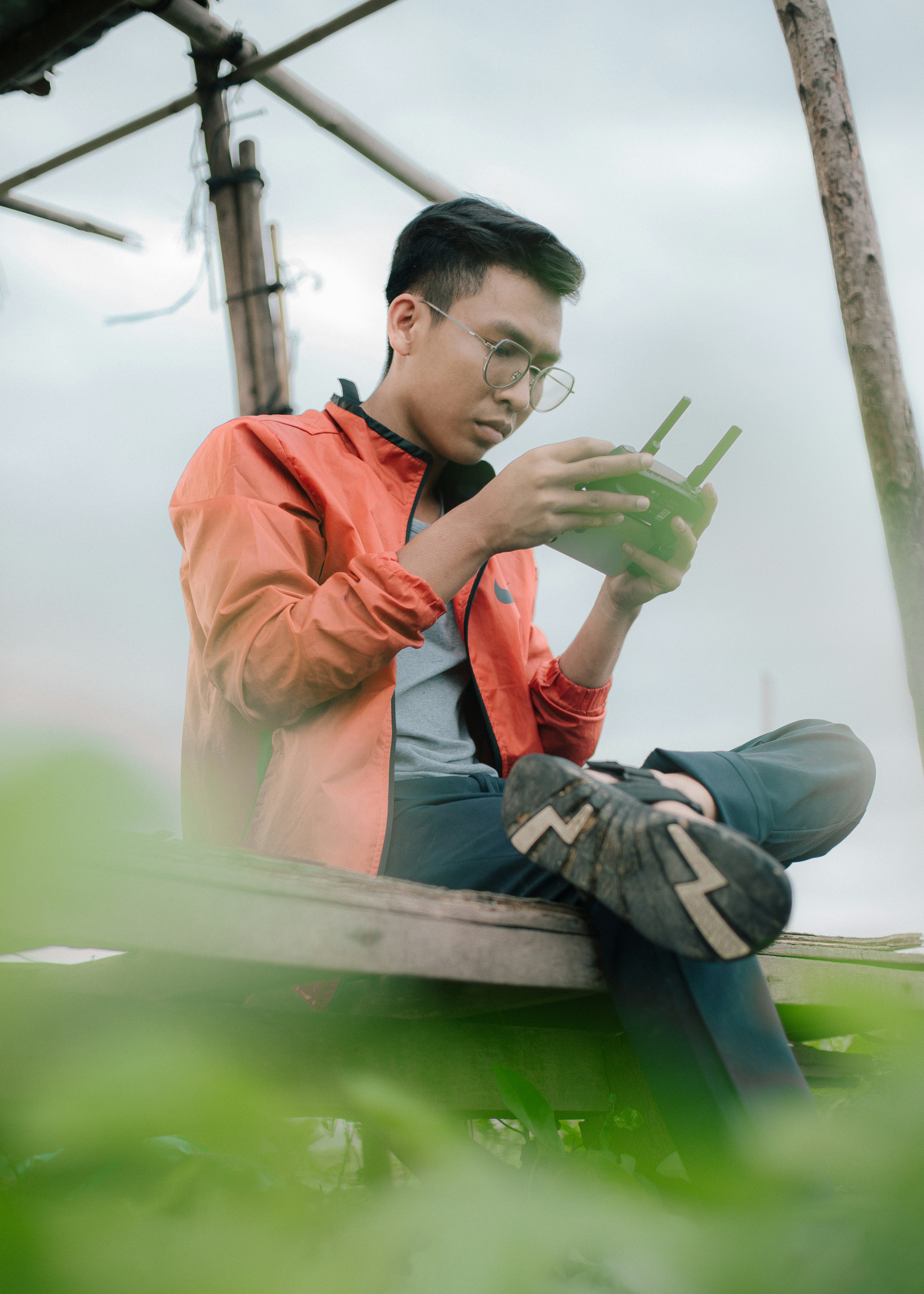 man in orange jacket and gray denim jeans sitting on green wooden bench